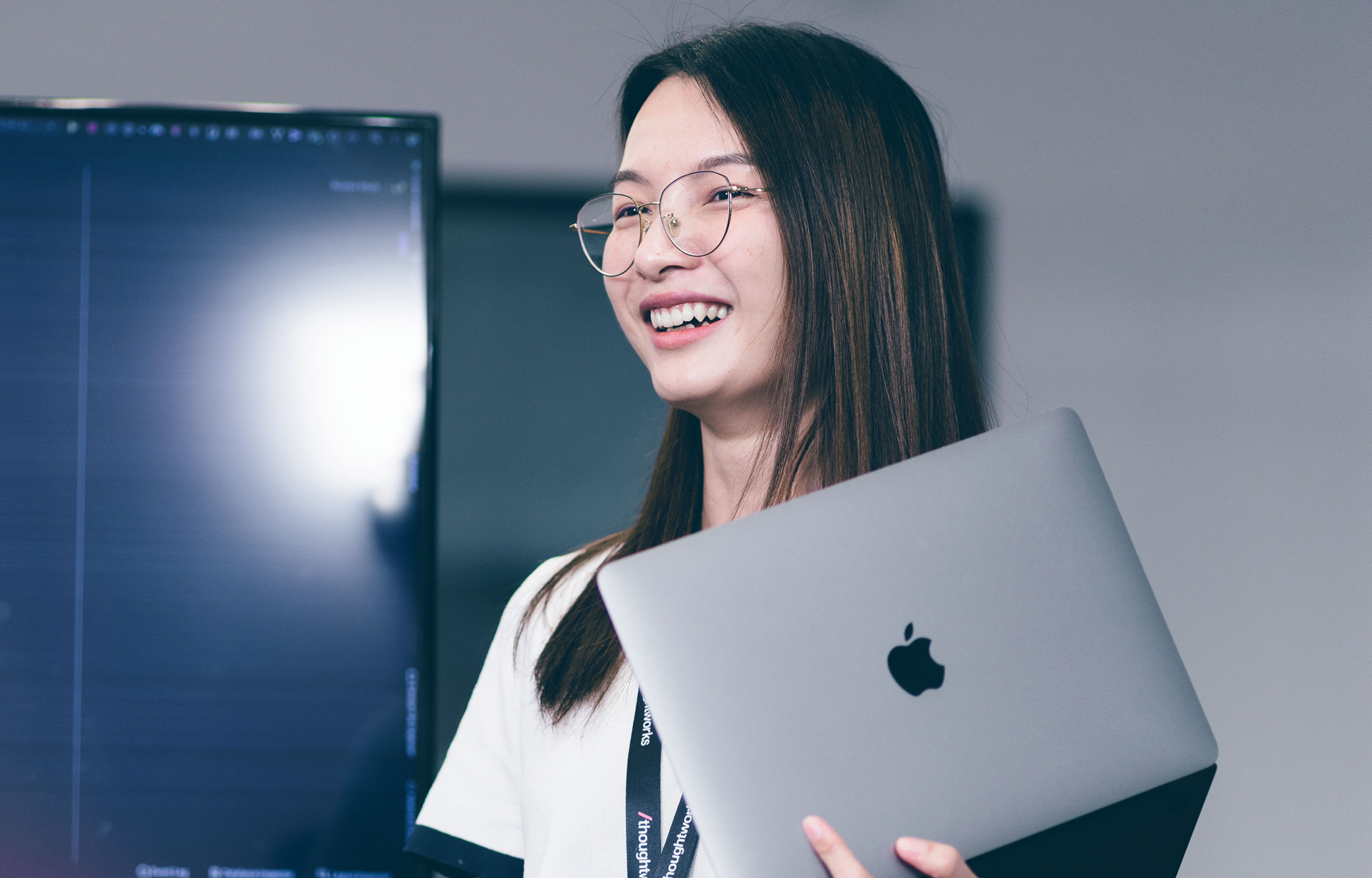 Image of a Thoughtworker smiling at the camera while holding a MacBook. Image of a Thoughtworker smiling at the camera while holding a MacBook.